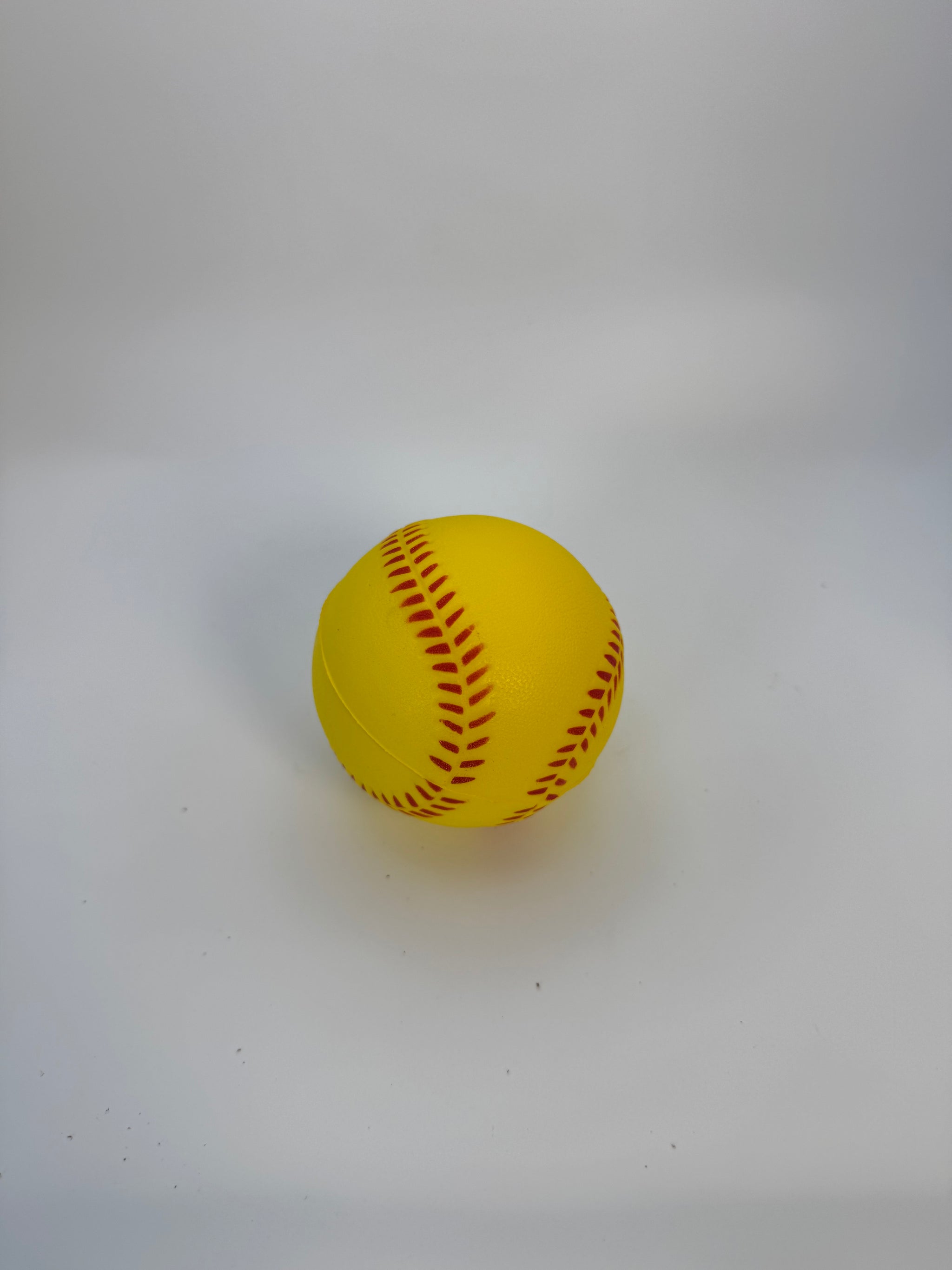 Yellow softball with red stitching on a white background